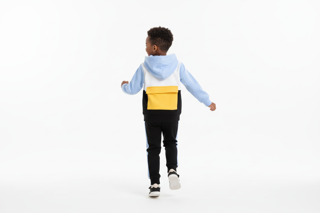 Vue arrière d'un enfant  portant un hoodie color block blanc, bleu ciel, jaune et noir avec pantalon noir à bandes bleues
