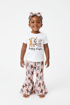 	Fillette debout en ensemble Happy Easter BabyCoton — t-shirt blanc lapins léopard, pantalon évasé rose lapins et bandeau nœud léopard, fond blanc