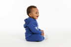 Vue de profil d'un bébé garçon d'origine diverse portant un body hoodie bleu avec texte KING et couronne blanc et pantalon bleu assorti
