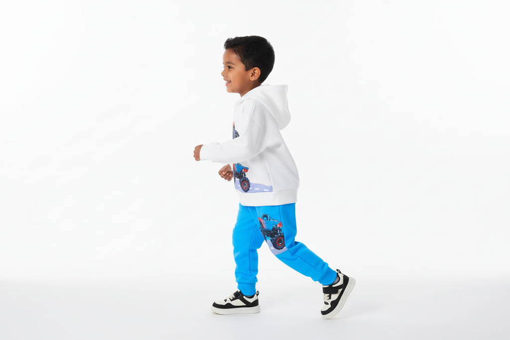 Vue de profil d'un garçon d'origine diverse portant un hoodie blanc avec motifs monster trucks colorés et pantalon bleu assorti
