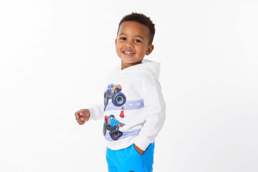 Vue trois-quarts d'un garçon portant un hoodie blanc avec motifs monster trucks colorés et pantalon bleu assorti
